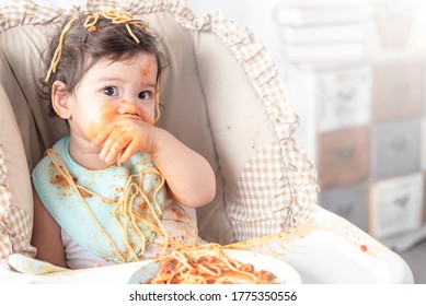 Lovely Baby Girl Eating Spaghetti And Making A Mess. Family Leave Baby Alone, Eating Pasta Herself.