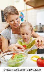 Lovely baby girl helping mother with meal in the kitchen. Young smiling female with little daughter cooking vegetables for family dinner.  - Shutterstock ID 310716290