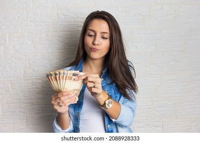 Lovely beautiful girl is holding a large amount of cash, a lot of money from Brazil. Business, income, loan, pay, buy, wealth concept.