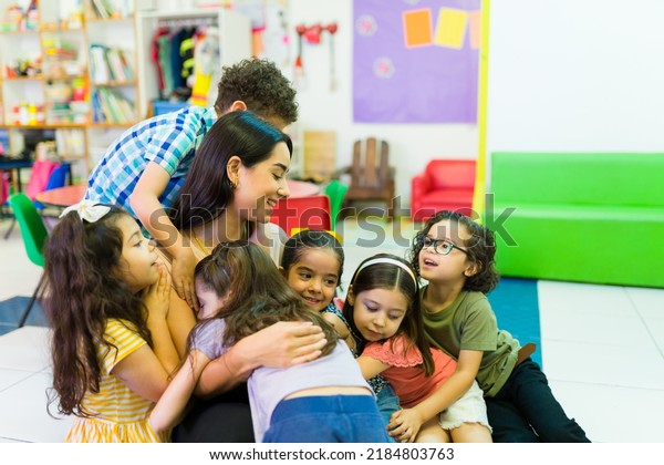 Lovely beautiful\
preschool teacher hugging her kindergarten students and enjoying\
coming back to school 