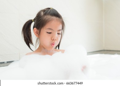 lovely beauty little girl sitting in bathtub with many bubble and using hands holding foam blowing let its splashing enjoying game time.