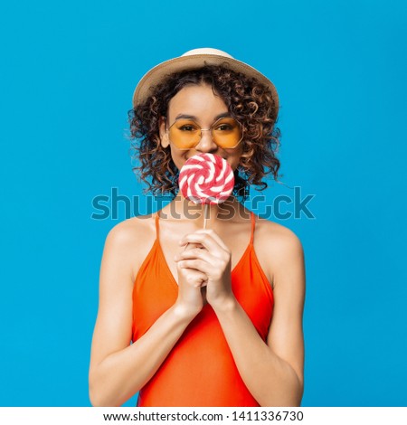 Lovely black girl eating big colorful lollipop, blue studio background