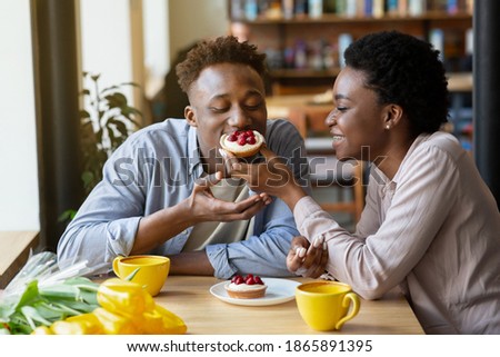 Lovely black woman feeding tasty berry tartlet to her boyfriend at cozy city cafe. Affectionate African American couple having dessert and coffee at restaurant, enjoying their first date
