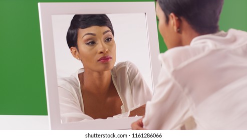 Lovely Black Woman Looking At Her Reflection In Mirror On Green Screen