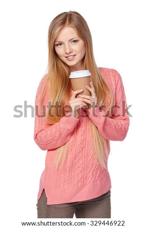 Lovely blond female in pink knit sweater standing casually holding a drink in disposable paper cup over white studio background