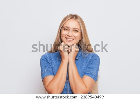 Lovely blonde girl with glasses wearing blue denim dress smiling gently isolated on background, happy life concept, copy space