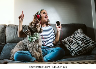 Lovely brown dog singing with her owner at home, sitting on the sofa. Funny time together. Lifestyle photography.