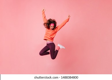 Lovely Brunette Girl In Pink Sports Headband And Tracksuit Jumps On Isolated Pink Background