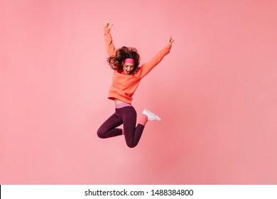 Lovely brunette girl in pink sports headband and tracksuit jumps on isolated pink background - Powered by Shutterstock