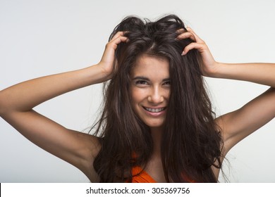 Lovely Brunette Is Holding Her Thick Hair On The White Background. Merry Woman In Orange Shirt Is Smiling.