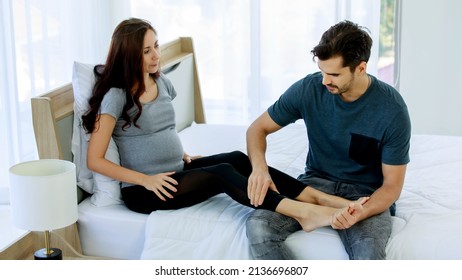 Lovely Caucasian husband do prenatal massage on legs of beloved pregnant wife with maternity care on bed to release stress and muscle pain while mom tenderly embrace belly of expecting unborn baby.