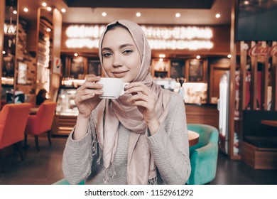 lovely charming Muslim girl with a headscarf sitting in a cozy cafe and drinking fragrant coffee - Powered by Shutterstock