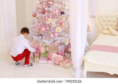 Lovely Children, Two Brothers Come With Gift Boxes To New Year Tree And Put Gifts For Parents, Show Concern And Desire To Congratulate Mom And Dad On Winter Holidays. Guys Of European Appearance With