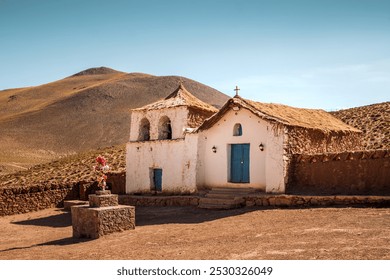 The lovely church of Machuca, a small village at 4000m of altitude near San Pedro de Atacama in Chile. The church features traditional adobe architecture including thatched roof and blue doors.