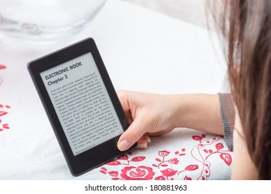 Lovely close up of e-book reader which is held by a young brunette girl during her reading time with, below, a beautiful background of an italian tablecloth.