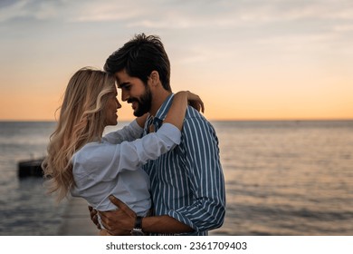 Lovely couple bonding at the beach in summer. Romantic male and female looking each other into eyes during the sunset. Beautiful couple in love standing face to face.
