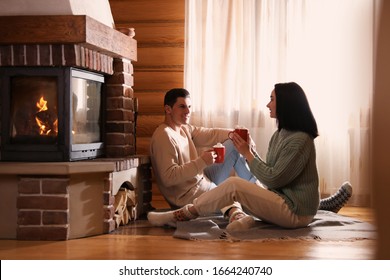 Lovely Couple With Delicious Cocoa Near Fireplace On Floor At Home. Winter Vacation