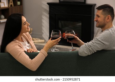 Lovely Couple With Glasses Of Wine Spending Time Together On Sofa Near Fireplace At Home