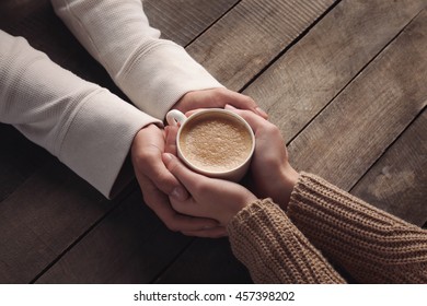 Lovely couple holding cup of coffee in hands on wooden background - Powered by Shutterstock