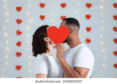 Lovely couple kissing behind red paper heart indoors. Valentine's day celebration - Shutterstock ID 2260343353