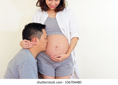 Lovely Couple In Love. Man Kissing Belly Of His Wife. Motherhood Concept. Mom And Dad Waiting For Newborn Baby.