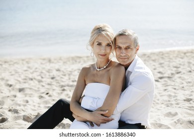 Lovely couple portrait on the ocean coastline which is sitting on the sand on the sunny summer day