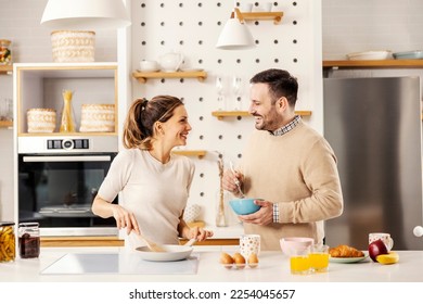 A lovely couple is preparing scrambled eggs is the morning for breakfast at home and smiling at each other. - Powered by Shutterstock