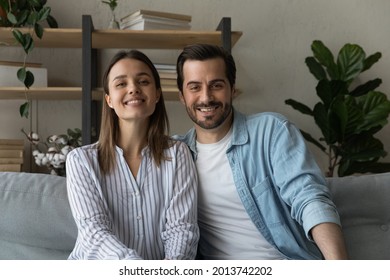 Lovely Couple Sit On Sofa Look At Camera, Videoconferencing Enjoy Chat With Family Living Abroad Use Global Remote Communication Video Call App. Virtual Meeting, Online Counselling For Spouses Concept