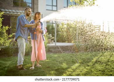 Lovely couple watering lawn at backyard of their country house on sunset. Young family taking care of their garden spending summer time together - Powered by Shutterstock