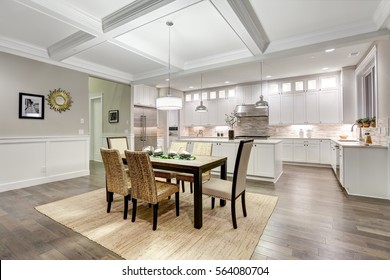 Lovely craftsman style dining and kitchen room interior with coffered cealing over rustic wooden dining table surrounded by wicker chairs. Northwest, USA
