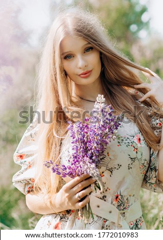 Lovely cute woman in lupine field with bouquet in hands, sunny day