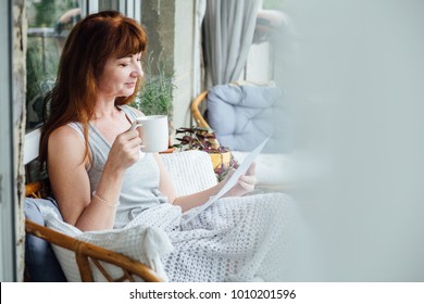 Lovely dreaming middle-aged redhead woman relaxing on balcony with plaid and cup of tea. - Powered by Shutterstock