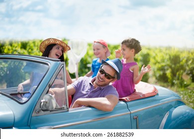 A Lovely Family Is Going On Vacation In A Convertible Retro Car. They Drive On A Country Road On A Sunny Day