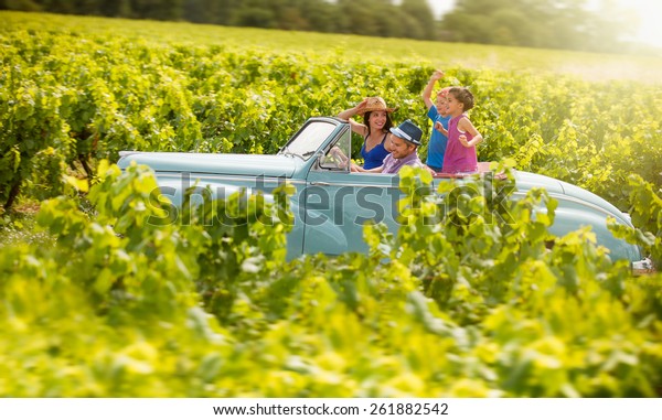 A lovely family is\
going on vacation in a convertible retro car, they drive on a\
country road on a sunny day