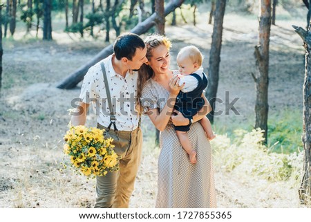 Lovely family walking in the summer forest. Happy parents enjoying fresh air and beautiful nature, holding hands, talking, smiling and laughing. Healthy lifestyle. Parents looking to son and talking