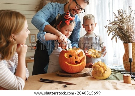Lovely father dad helping little daughter to remove all the pulp from pumpkin while carving jack o lantern with family in cozy kitchen at home, parents with kids preparing for Halloween