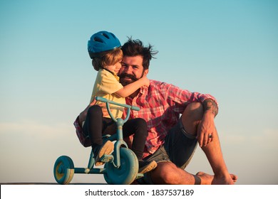 Lovely Father Teaching Son Riding Bike. Happy Dad Helping Excited Son To Ride A Bicycle. Young Smiling Boy Wearing Helmet While Learning To Ride Cycle With His Daddy