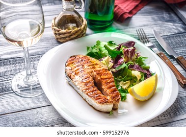 Lovely fish steak with salad, lemon and white wine on a wooden table