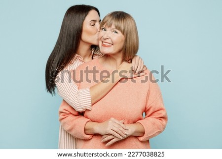 Lovely fun smiling happy caucasian elder parent mom with young adult daughter two women together wearing casual clothes hugging cuddle kiss isolated on plain blue cyan background. Family day concept