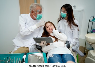 Lovely girl children lie on dental clinic chair and wait for treatment during senior dentist discuss with staff.