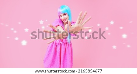 A lovely girl with colored purple-blue hair and pink dress spreads magic stars with her hands. Studio portrait on a pink background. Hairstyle, hair coloring. Make-up and cosmetics.
