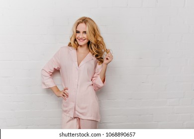 Lovely girl in cotton pyjama playing with her wavy hair. Studio portrait of laughing woman in pink night-suit smiling on white background. - Powered by Shutterstock