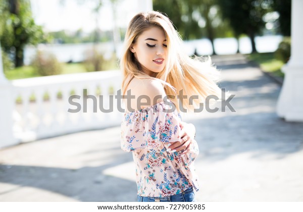 Lovely\
girl with curly hair waving walking down the street and looking\
around with smile. Cheerful fair-haired young woman spending time\
outdoor carrying little backpack on one\
shoulder.