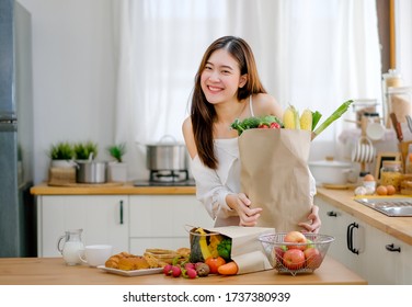 Schönes Mädchen halten Tasche mit verschiedenen Gemüse und Lächeln stehen in der Küche und sehen glücklich in der Morgenlicht. Konzept der gesunden Lebensmittel für ein gutes und besseres Gesundheitsmanagement während der Arbeit von zu Hause aus.