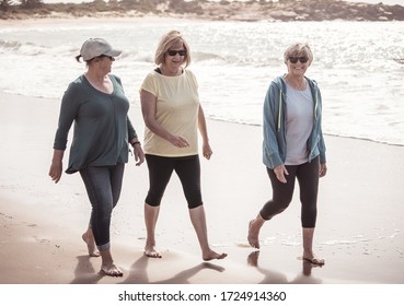 Lovely Group Of Three Active Senior Woman On Their 60s Walking, Exercising And Having Fun On The Beach. Mature Females Laughing Enjoying Walk On Vacation. Retirement And Health Lifestyle.