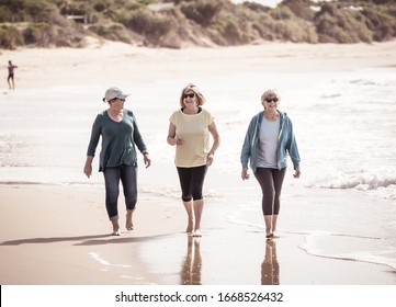 Lovely Group Of Three Senior Retired Woman On Their 60s Walking And Having Fun On Holiday Beach. Mature Females Laughing Enjoying Friendship. In Vacations And Retirement Lifestyle Concept.