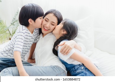 Lovely Happy Asian Family At Cozy Home. Son And Daughter Kiss Mother With Enjoy ,relax And Playful Together In Bedroom. Happiness Relationship And Bonding Of Love Between Parent And Children Moment

