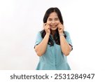 Lovely happy Asian lady keeps hands on cheeks smiles sincerely has soft healthy skin wears casual shirt poses indoor. Pleasant human emotions and face expressions