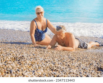 Lovely happy middle aged couple is sitting on the stone seashore. Sea and rocky beach. Happy couple, elderly people rest together by the sea, love, lifestyle. - Powered by Shutterstock