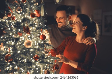 A lovely happy young adult couple bonding while decorating the glowing Christmas tree on cozy Christmas Eve. - Powered by Shutterstock